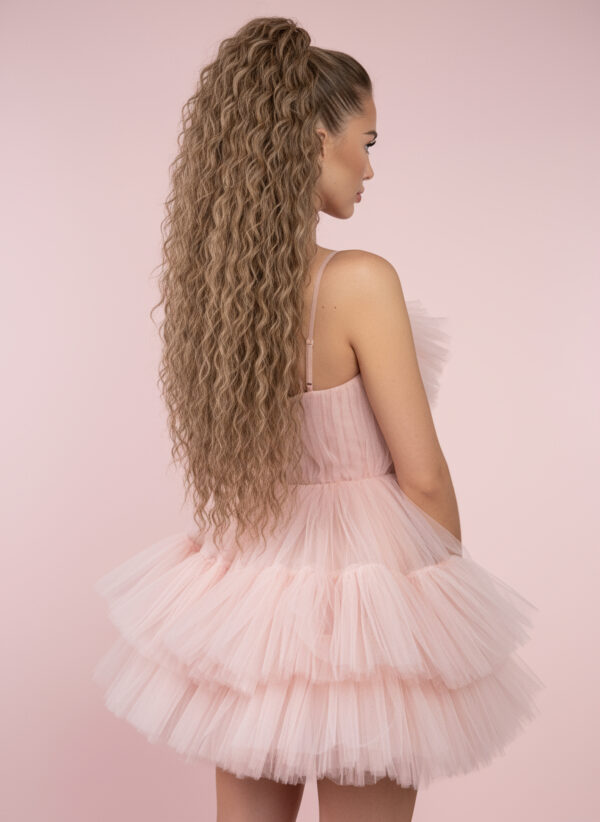 Create a glamorous, fashion-editorial style image inspired by Barbie aesthetics, focusing on the hairstyle. Show a woman from the back or three-quarter view against a solid pink background, wearing a soft-pink fluffy robe with tulle texture. The lighting highlights the hair — a high, long, curly blonde ponytail with tight, defined waves and glossy shine, matching the reference ponytail’s color and texture. The model’s face and makeup are subtle and secondary, softly blurred or minimally shown. Emphasize the ponytail’s volume, curl definition, and luxurious texture. Overall mood: chic, feminine, and playful, like a beauty product campaign that showcases the ponytail as the centerpiece
